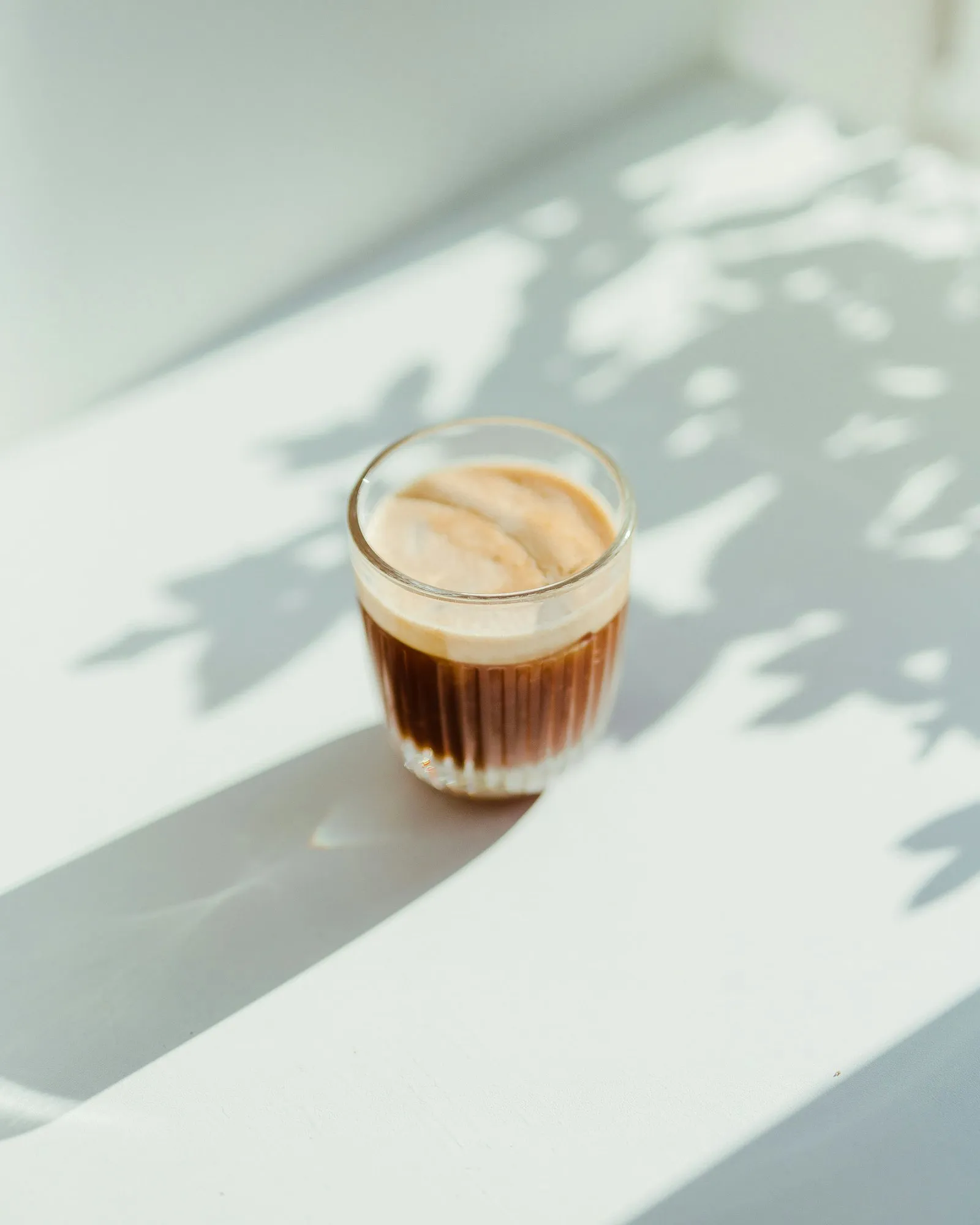 Pahar de cafea în lumină moale, filtrată prin frunze